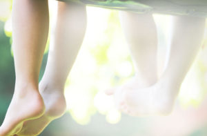 Close-up of two people’s bare legs and feet dangling in sunlight, with a soft, warm, and peaceful outdoor background